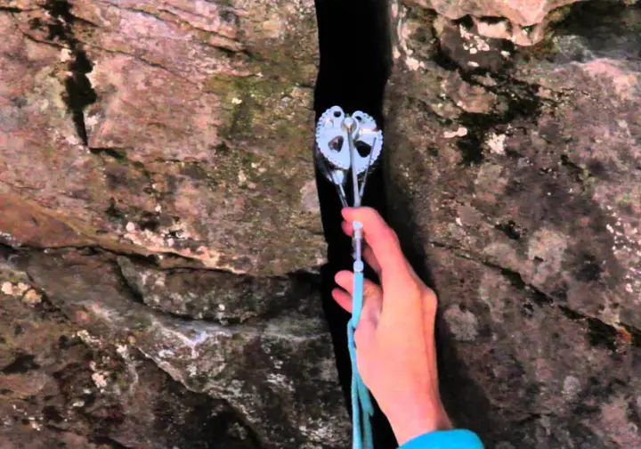 Close-up of a climber's hands expertly placing a cam in a challenging flared or horizontal granite crack, demonstrating cam mastery and advanced techniques for active protection.