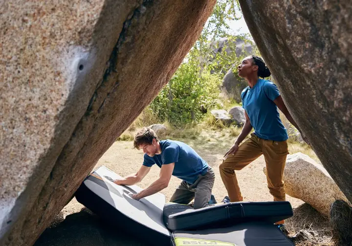 Two climbers effectively placing and overlapping bouldering crash pads at the base of a boulder to maximize safety and confidence.