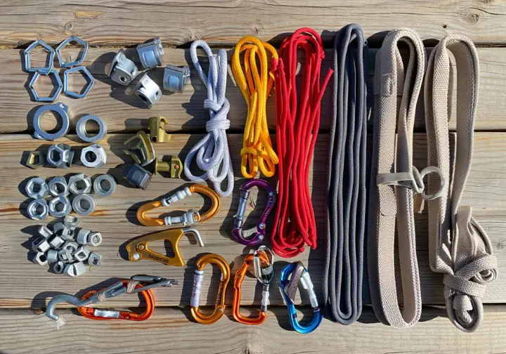 Flat lay of essential gear for building bombproof trad anchors: cams, nuts, hexes, various slings, cordelette, locking carabiners, and a nut tool, meticulously arranged.