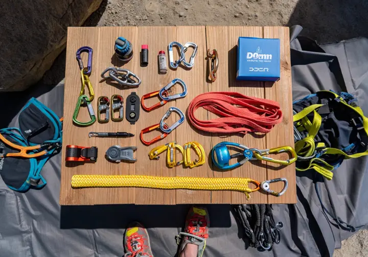 Flat lay of essential gear for a first trad climbing rack, including nuts, cams, alpine draws, locking carabiners, and a nut tool, neatly arranged for gearing up.