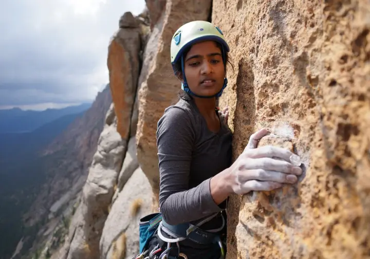 A climber on an exposed alpine route, looking thoughtful and fatigued as weather changes, highlighting human factors and system vulnerabilities in climbing.
