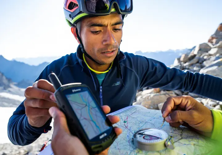 Alpinist in alpine terrain effectively integrating GPS technology by cross-referencing a handheld GPS unit displaying a map with a physical topographic map and compass.