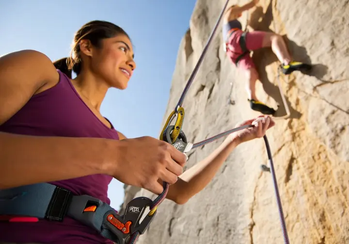 Skilled climber expertly lead belaying, demonstrating essential ropework techniques like smooth slack management with a belay device for sport climbing safety.