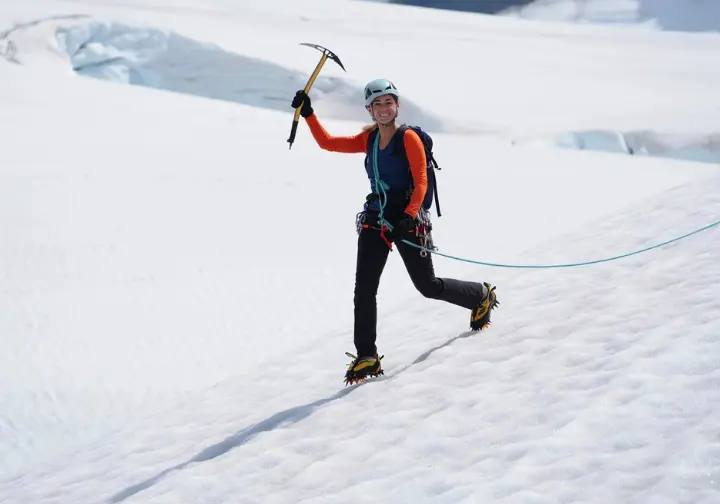 Alpinist demonstrating foundational glacier travel techniques: using French technique (flat-footing) with crampons and piolet canne with an ice axe on a snowy glacier slope.