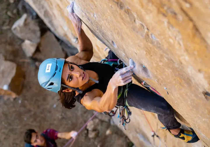 Climber intently working a crux sequence on her outdoor sport climbing project, analyzing holds and using redpoint tactics to master the route.