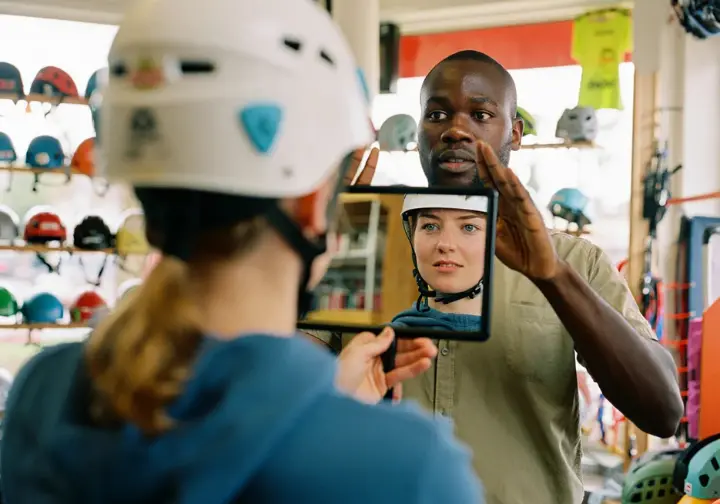 Gear shop employee guiding a customer through the step-by-step process of achieving the perfect climbing helmet fit.