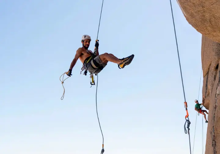 Climber rappelling with a clearly visible friction hitch backup and stopper knots on rope ends, demonstrating prevention of rappelling accidents.