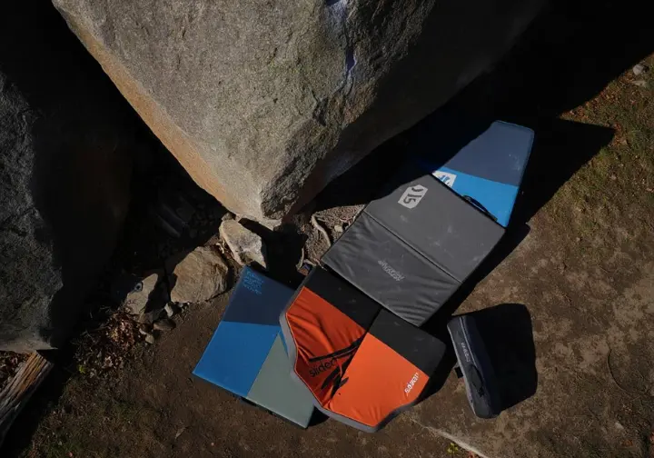 Multiple crash pads strategically arranged and overlapped at the base of an outdoor boulder, covering an uneven landing zone for optimal bouldering protection.