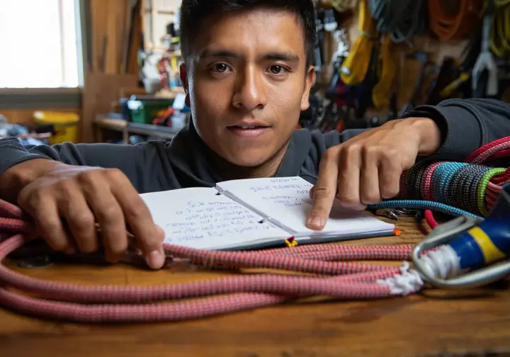 A climber pointing to critical damage on an old climbing rope next to a logbook, making the decision for its retirement, part of the ultimate guide.
