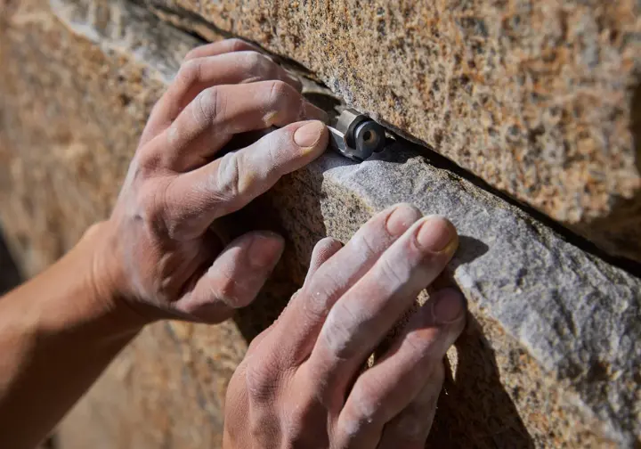 Close-up of a climber's hands assessing rock quality and a perfectly placed trad cam in a granite crack, illustrating the art and core principles of solid protection.