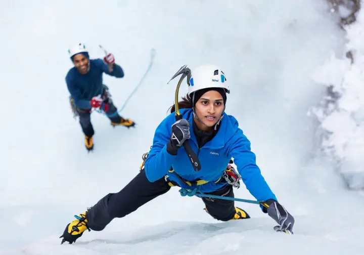 Beginner ice climber demonstrating a foundational technique like the "A-Frame" stance with secure ice tool and crampon placement on a low-angled ice wall, making her first moves.