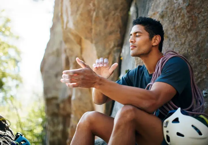 Climber at the base of a sport route with closed eyes, pantomiming moves, using visualization, sequencing, and memory—the mind's eye—for route reading