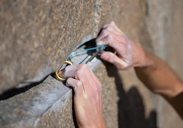 Extreme close-up of a perfectly placed nut (stopper) securely wedged in a granite crack, with hands giving it a final setting tug, showcasing nutcraft excellence in trad climbing.