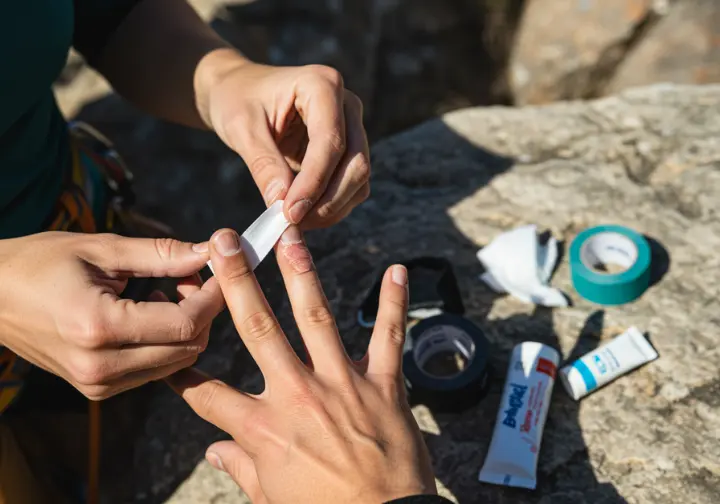 Close-up of a climber's hands carefully applying climbing tape to treat a finger flapper, demonstrating practical first aid for common climbing injuries.