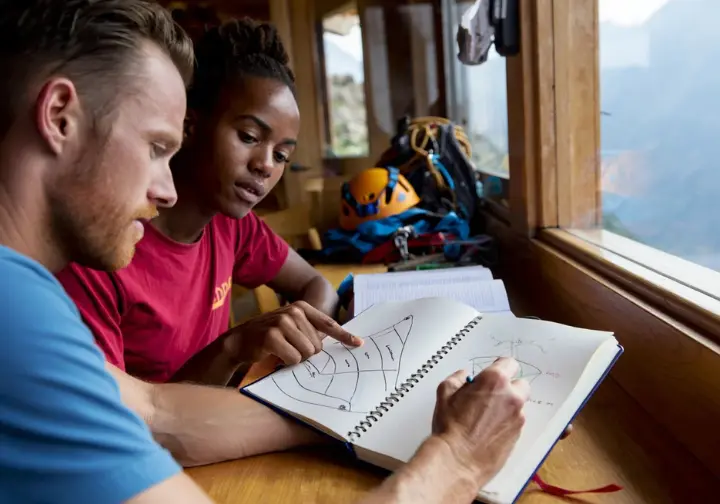 Two diverse climbers analyzing a climbing incident using a Swiss Cheese Model sketch in a journal, showing real-world application of the SCM.