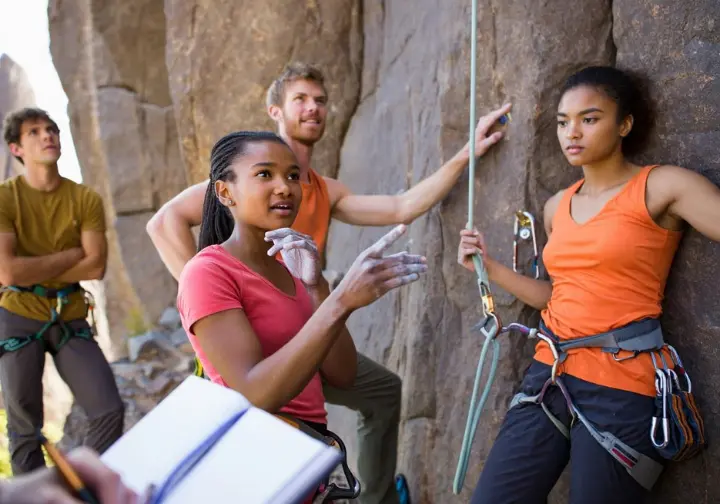 First ascensionist discussing a newly bolted sport route with other climbers at the crag, gesturing towards the rock, illustrating the subjective science of how routes get their grades.