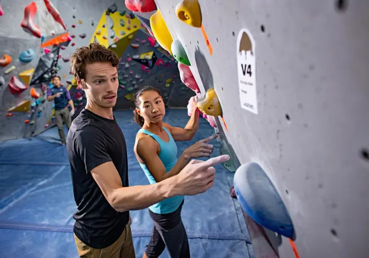 Two climbers of different builds discussing the difficulty of the same graded bouldering problem, illustrating the subjectivity factor in climbing grades.