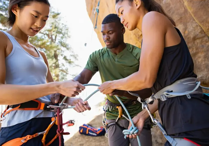 Two diverse climbers performing a meticulous pre-climb partner check, examining knots, harnesses, and belay system, illustrating systemic safety protocols for sport climbing.