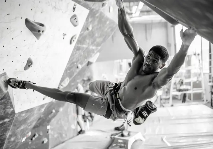 Boulderer mid-air executing an explosive dyno on a campus board or system wall, training to unleash powerful bouldering movements.