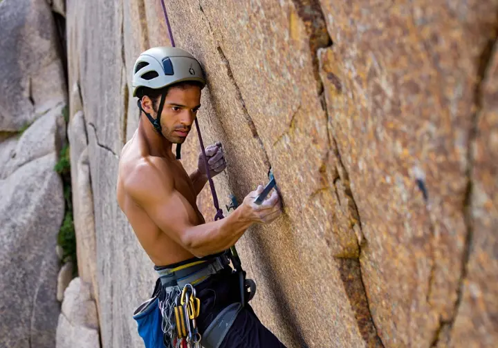 Experienced trad climber using judgment and cliff sense to assess a complex or unconventional anchor placement on a granite cliff, going beyond basic acronyms for trad anchors.