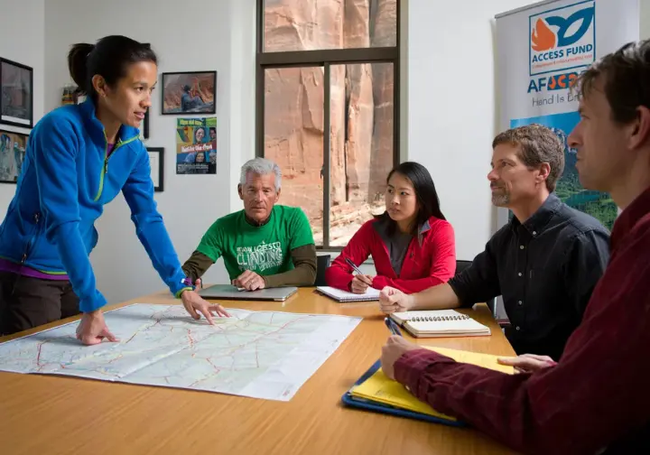 Diverse group of climbers engaged in an advocacy meeting, discussing maps and strategies for protecting climbing access and ensuring the future of climbing.