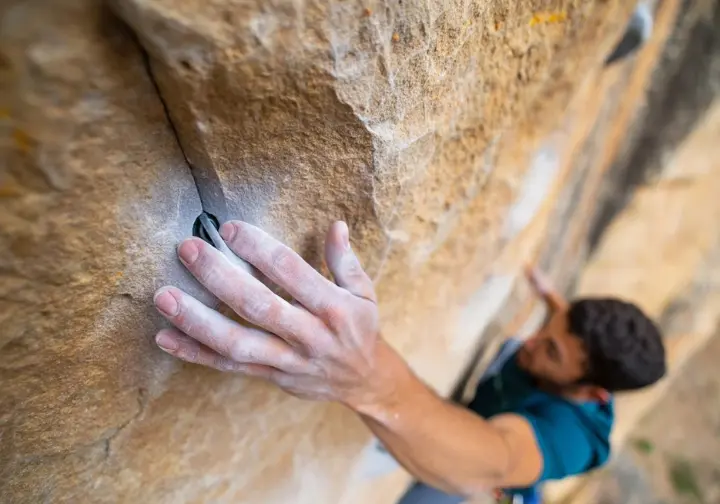 Close-up of a climber's hand pointing to specific holds and features on a rock face, illustrating the process of decoding a sport climb to identify rests and plan pacing strategies.