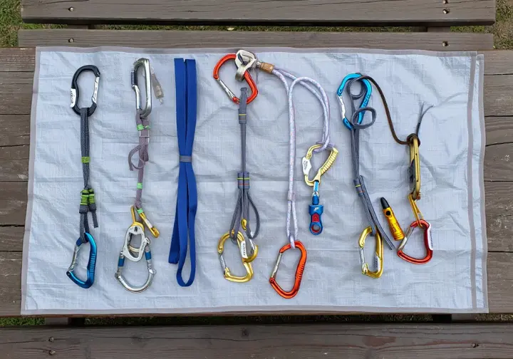 Flat lay of essential trad climbing slings (alpine draws, double-length, cordelette) and carabiners (non-locking and locking), crucial connectors and extensions.