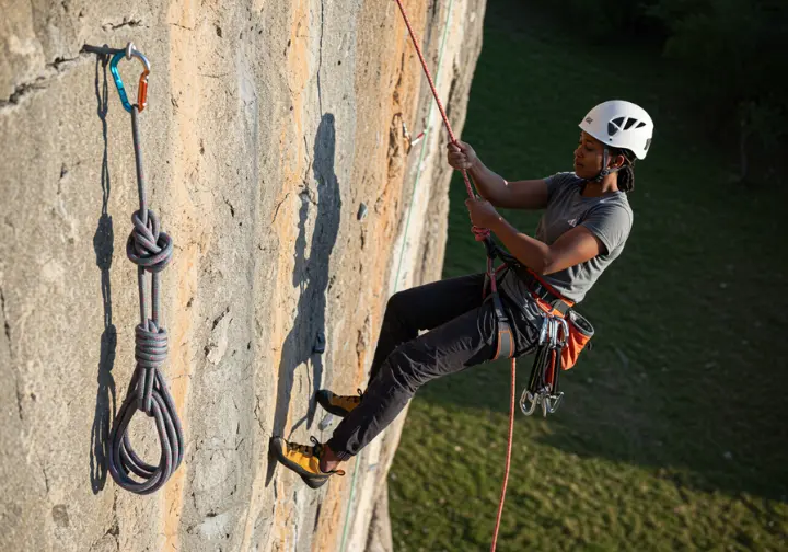 Climber ascending a fixed rope using a two-friction-hitch system (Prusik and Klemheist with foot loop), demonstrating a self-rescue technique.
