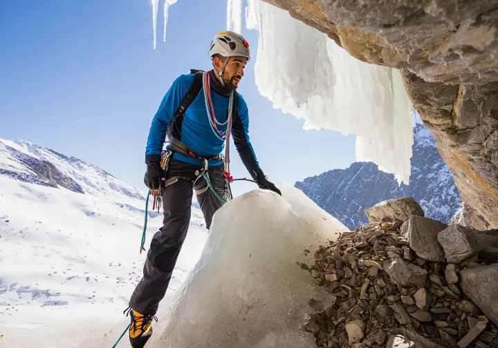 Ice climber carefully navigating past an objective hazard like a large detached icicle or under an avalanche-prone slope, demonstrating risk management in ice climbing.