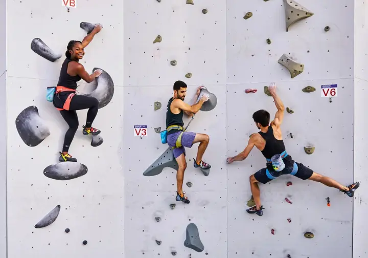 Three climbers on an indoor wall demonstrating characteristics of beginner, intermediate, and advanced gym grades, a practical guide to what to expect.