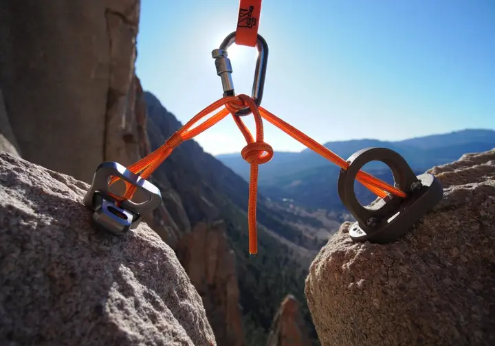 A perfectly constructed three-piece trad climbing anchor on a granite cliff, showcasing SERENE principles with cams, nuts, and an equalized cordelette master point.