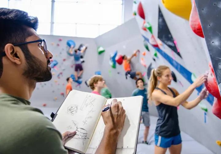 Climber thoughtfully analyzing a route with a notebook, while others discuss beta, illustrating the climber's toolkit for engaging with grades intelligently.