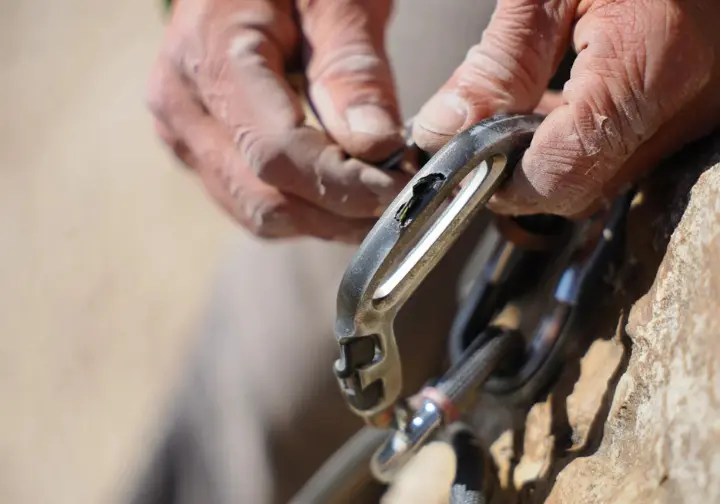 Close-up of hands inspecting a dangerously worn climbing carabiner with a deep rope groove, illustrating gear failure prevention.