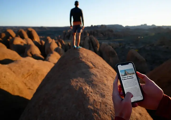 A boulderer contemplates the Hueco Tanks landscape, with a foreground element questioning the 2025 Rock Rodeo, addressing its ambiguous status.