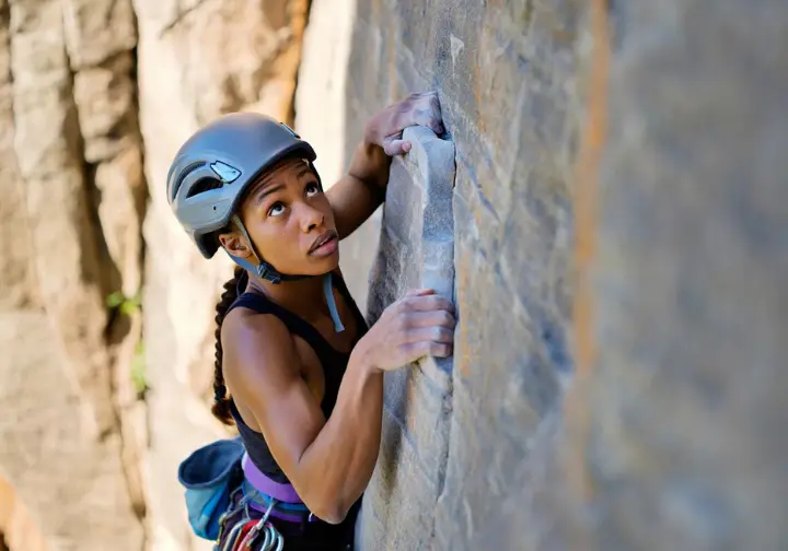 Climber paused mid-route on a challenging outdoor sport climb, thoughtfully assessing the holds above, illustrating the mental game and progression in climbing.