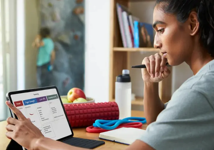 Climber thoughtfully reviewing a periodized bouldering training plan on a tablet, with supporting elements like a foam roller and resistance bands nearby, illustrating structured training.