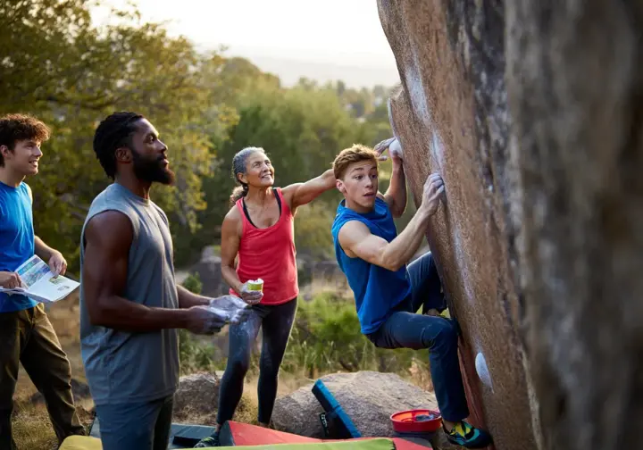 Diverse group of boulderers interacting positively at an outdoor crag or indoor gym, spotting, sharing beta, and brushing holds, embodying bouldering culture, ethics, and community.