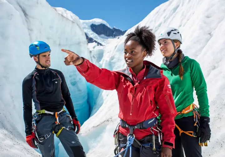 Mountain guide instructing two competent alpinists on advanced crevasse rescue techniques or hazard assessment on a glacier, symbolizing continuous learning and advanced considerations.