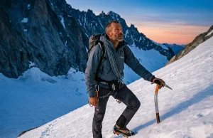 7 Alpine Climbing Skills That Actually Keep You Safe Alpine climber in cane position on steep snow slope holding Petzl ice axe, mountains at dawn