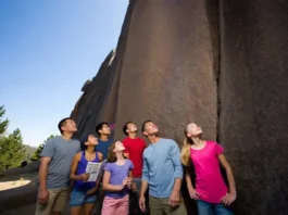 A diverse group of climbers at the base of a large rock face, looking at routes and maps, symbolizing the process of choosing the best outdoor rock climbing camp.