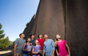 Choosing a Climbing Camp: A Guide to Finding the Best A diverse group of climbers at the base of a large rock face, looking at routes and maps, symbolizing the process of choosing the best outdoor rock climbing camp.
