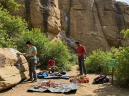 Diverse climbers practicing Leave No Trace ethics at a pristine crag, including brushing holds and using a rope tarp, for a guide to LNT.