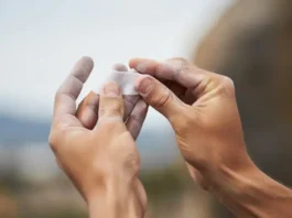 A climber's hands applying white rock climbing finger tape to a finger, illustrating skin protection and pulley support techniques.