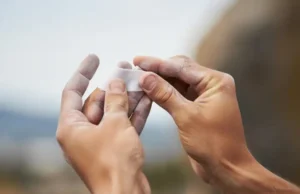 The Climber’s Taping Playbook: For Pulleys & Skin A climber's hands applying white rock climbing finger tape to a finger, illustrating skin protection and pulley support techniques.