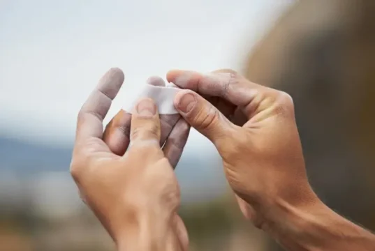 The Climber’s Taping Playbook: For Pulleys & Skin A climber's hands applying white rock climbing finger tape to a finger, illustrating skin protection and pulley support techniques.