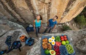 Climbing Nutrition: The Ultimate High Protein Low Carb Foods List A male and female climber prepare at a sunny rock face, with a high protein low carb food selection laid out for energy.