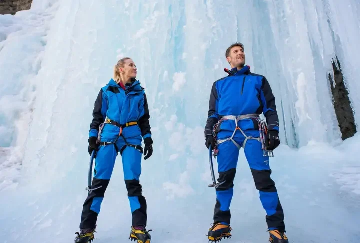 Two ice climbers with a complete gear system standing before a large frozen waterfall, ready for a climb.