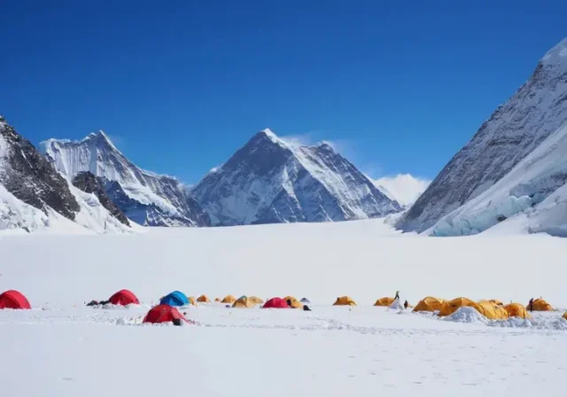 Photorealistic image of Mount Everest's Camp 1, showing colorful tents nestled in a snow-covered basin surrounded by towering peaks under a clear sky, highlighting its strategic location.