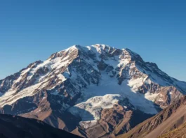 A majestic, wide-angle view of Mount Aconcagua, the highest mountain in the Americas, showing its snow-covered peak and visible climbing routes under a clear sky.