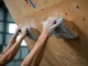 Mastering the Hangboard: A Beginner’s Training Plan Hands of two diverse climbers gripping a wooden hangboard, representing a beginner's training plan for finger strength in rock climbing.